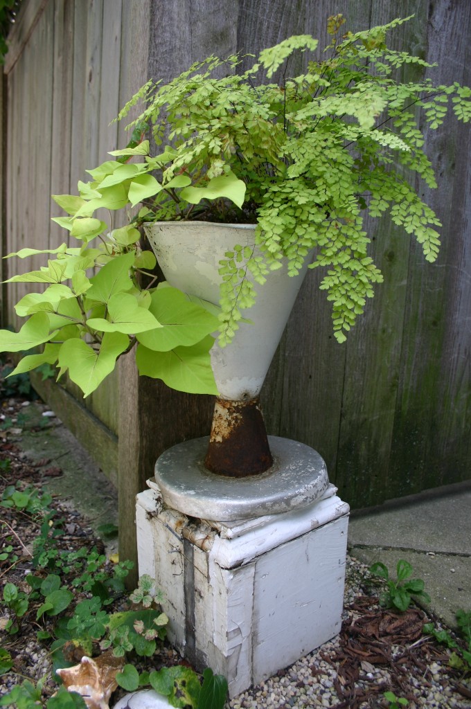 An umbrella stand is repurposed as a planter; it sits on the top of an old post. Combining the two pieces gave me the height I desired.