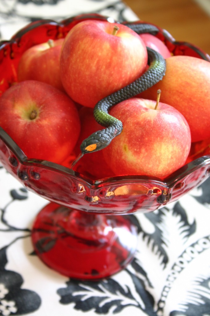 This red glass footed bowl holds apples and a rubber snake.