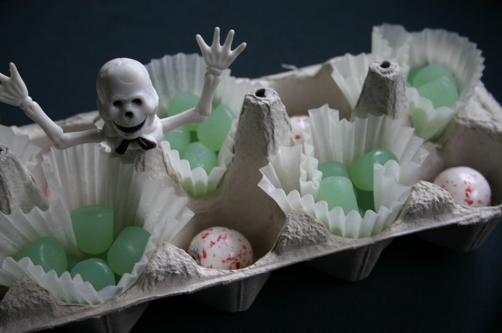An unpainted egg carton filled with Ghost Dots and Eyeball Gumballs and topped off with a skeleton finger puppet.