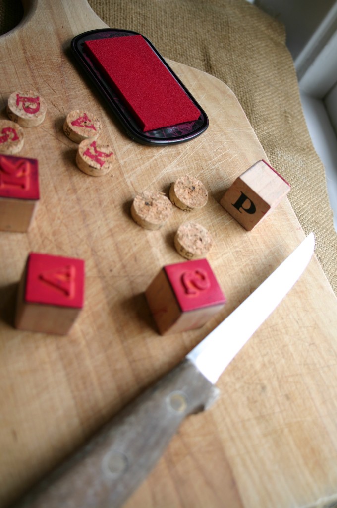 Using a sharp knife and a cutting board - cut the cork into 1/2 inch discs. Stamp each cork slice with a letter rubber stamp.