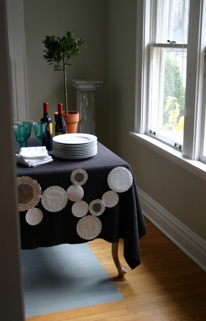 Silver and white paper doilies of varying sizes are stapled together to create a lacey tabletop cover for a winter dinner.