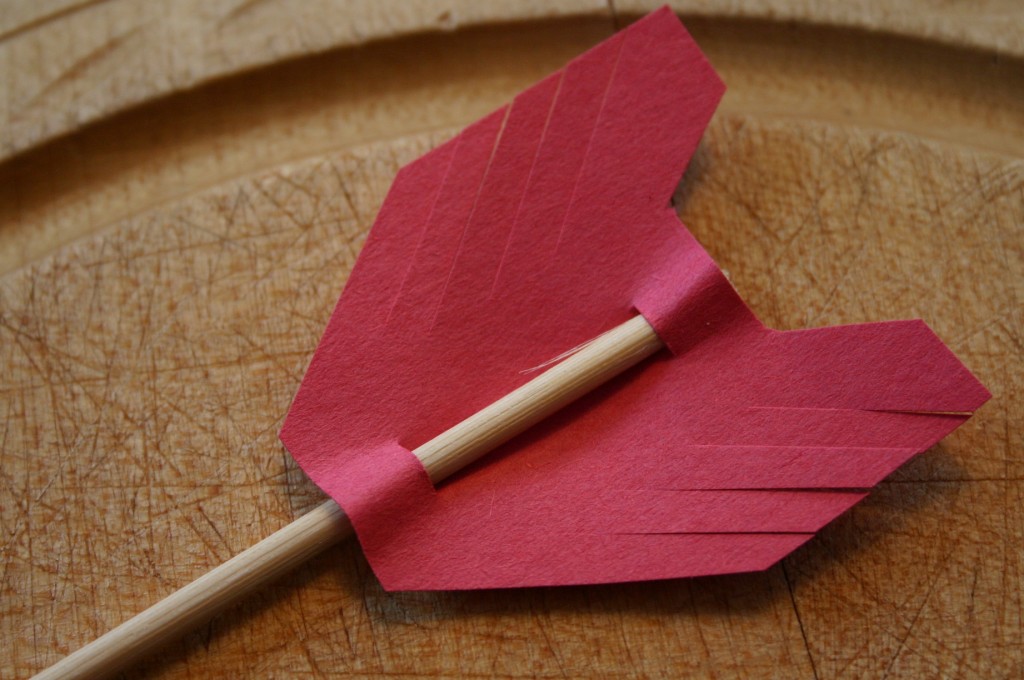 Cut an arrow tip and end out of red construction paper. Add two small slits to each shape so you can slip in a wooden skewer. I had a bag of 10" skewers that I cut down to 8". You can find these in the cooking supply aisle of your supermarket. 
